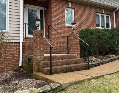 Simple black handrails beside a short flight of brick entry steps