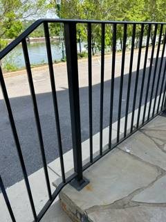 Simple black railing bordering a stone-paved entrance landing