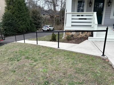 Simple black railings following a sloping concrete path across a lawn