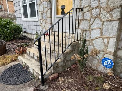 Simple black stair railing beside a stone-faced house entrance
