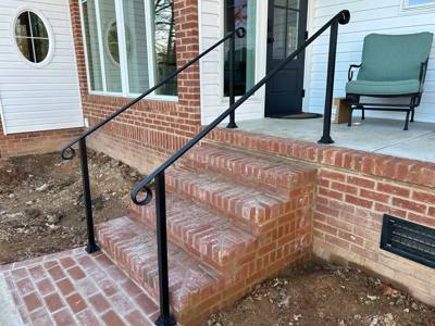 Slender black handrails with looped ends beside brick porch stairs