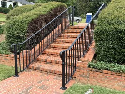 Slender black railing following brick garden stairs between trimmed hedges