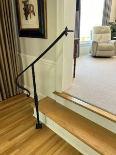 Slender black stair handrail with a turned post beside wooden steps
