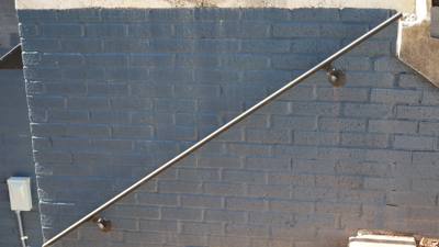Sloping wall-mounted metal handrail on a painted brick wall