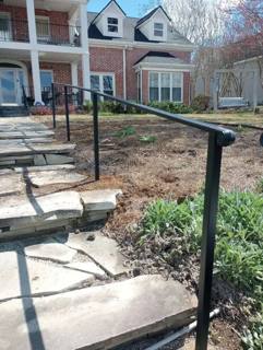 Straight black handrail following stone steps toward a landscaped porch