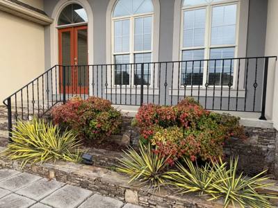 Straight black porch railing above a landscaped stone retaining wall