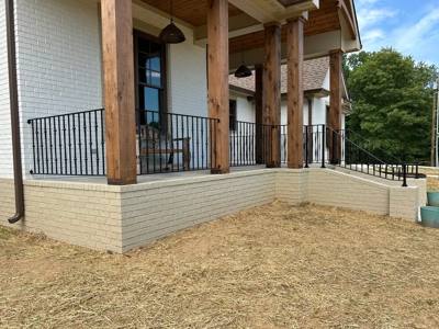 Straight black porch railing between timber posts above a pale brick wall
