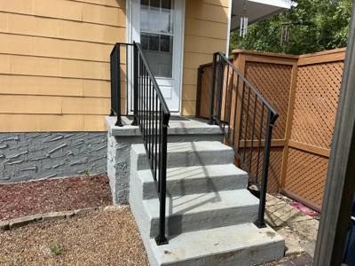 Straight black railings framing concrete side-entry steps beside a wooden fence