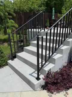 Straight black rails beside gray concrete steps and a landscaped bed