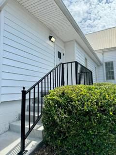 Straight black stair railing beside white siding and a rounded shrub