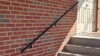 Straight wall-mounted black handrail beside concrete steps and brick wall