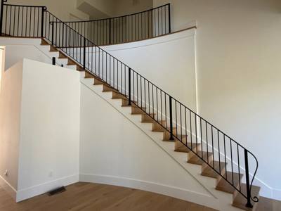 Sweeping wood staircase with black railings against a white curved wall