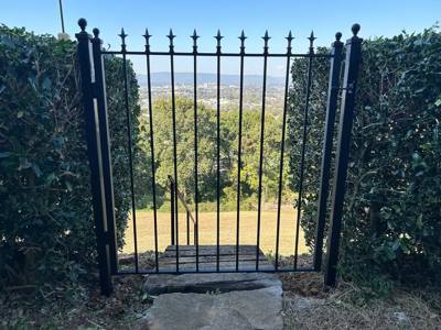 Tall black garden gate with pointed finials opening toward a hillside view