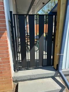 Tall black pedestrian gate with vertical slats in a narrow passage