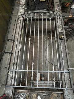 Unfinished arched gate with vertical pickets laid out in a workshop