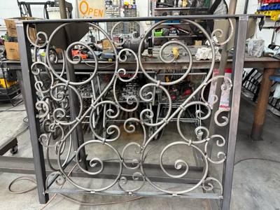 Unpainted ornamental gate with large circular scrolls in the workshop
