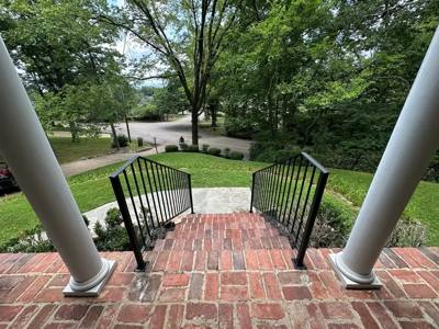 View down brick porch steps between black railings and white columns