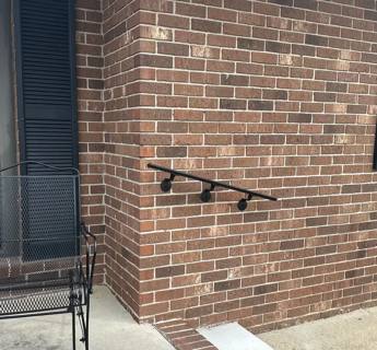 Wall-mounted black handrail on a brick wall beside outdoor steps