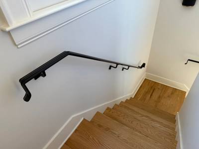 Wall-mounted black handrail turning at an indoor wooden stair landing