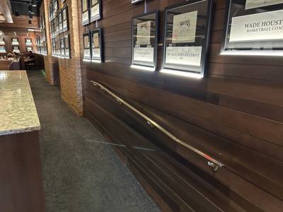 Wall-mounted handrail along a wood-paneled indoor passage beneath framed signs