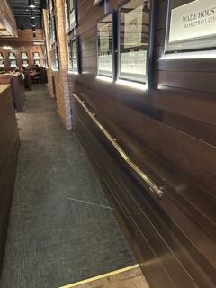 Wall-mounted handrail beneath framed displays on a wood-paneled interior wall