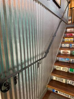 Wall-mounted handrail with a curled end beside a narrow interior staircase