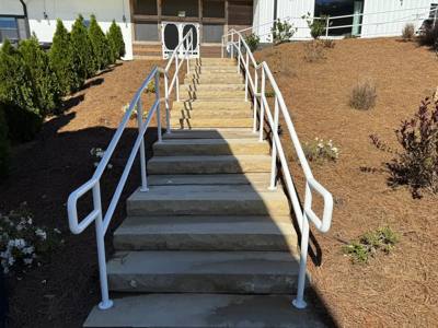White double-level handrails alongside a long concrete hillside stairway