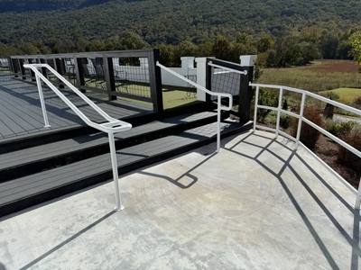 White handrails around the transition from gray deck steps to concrete paving