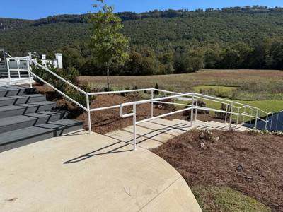 White handrails beside a concrete stair landing overlooking wooded hills