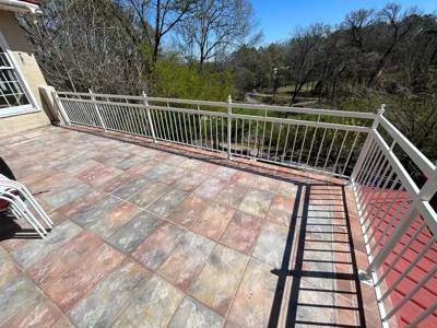 White railing surrounding a patterned tile patio with a distant tree-lined view