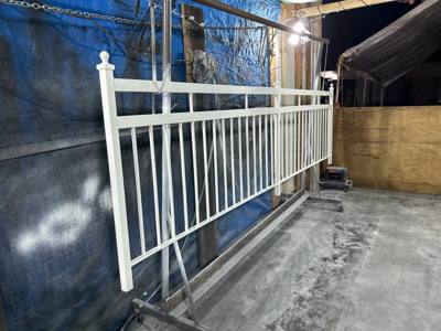White spear-top fence panel resting upright beside a workshop wall