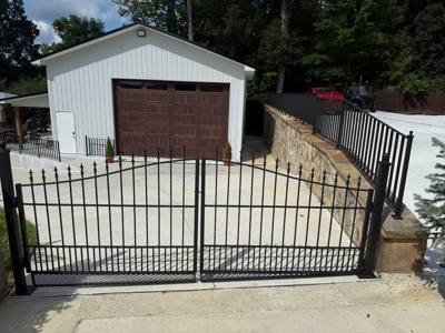 Wide black driveway gate spanning a concrete drive beside a garage