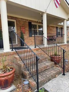 Wide stone porch stairs with black handrails and potted plants